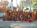 Una imagen festiva de niños y adultos vestidos con trajes tradicionales posando en una calle. En el fondo, se pueden ver edificios y árboles, lo que sugiere un entorno urbano. La celebración parece ser de una festividad o evento cultural importante, posiblemente relacionado con la tradición local.