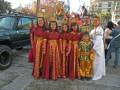 Una familia vestida con trajes tradicionales en una celebración festiva, con un auto y edificios en el fondo.