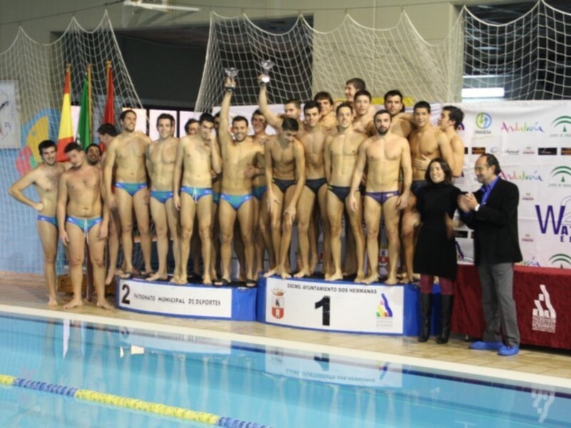 Equipo masculino de waterpolo celebrando en el podio, con banderas nacionales en el fondo y un trofeo en la mano central.