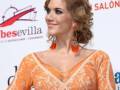 A una mujer con un vestido naranja y un peinado estilo flamenca, posiblemente en una gala o evento cultural.