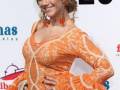 Una mujer con vestido naranja de flamenca, pendientes rojos y flores en el cabello.