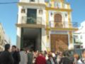 Una iglesia con una torre de campanas y un arco en la entrada, rodeada por personas que parecen estar esperando o participando en una actividad.