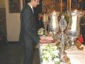 Persona en traje negro en una ceremonia religiosa con altares y velas iluminadas.
