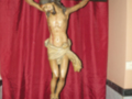 Estatua de Cristo crucificado en una iglesia, con un fondo de cortina roja y una inscripción en el fondo.