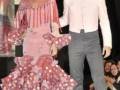 Una pareja en trajes tradicionales españoles, la mujer con un vestido de flamenca rosa y el hombre con un traje blanco.