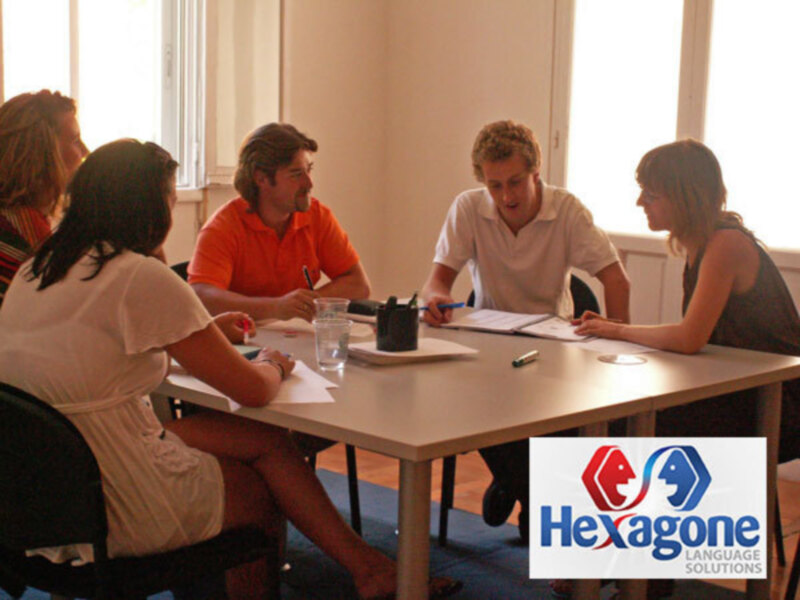 Gente reunida en una sala de conferencias, sosteniendo documentos y pluma. Imagen promocional para Hexagone Language Solutions.