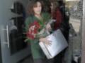 Una mujer con un ramo de flores rojas y una bolsa blanca sale de un edificio.