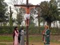Una cruz con un hombre crucificado, tres personas observan desde atrás. Contexto: escena religiosa o de devoción.