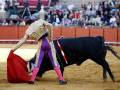 Un torero en traje tradicional lucha con un toro negro en una plaza de toros.