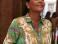 Mujer sonriente con blusa estampada de colores en un entorno interior.