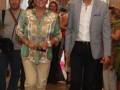 Personas en un evento formal, con una mujer en el centro luciendo un vestido floral y pantalones beige.