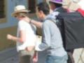Dos hombres con sombreros caminan por una calle, uno de ellos lleva un gran bolso negro.