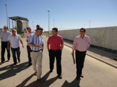 Un grupo de hombres camina y conversa en una zona industrial al aire libre bajo un cielo azul claro.
