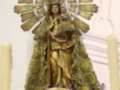 Elegante estatua de la Virgen María con un manto dorado y flores en la base, en una iglesia.