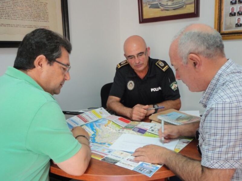 Tres personas sentadas en una mesa, con un mapa y un cuaderno en el centro, discutiendo sobre información relevante para el contenido visual.