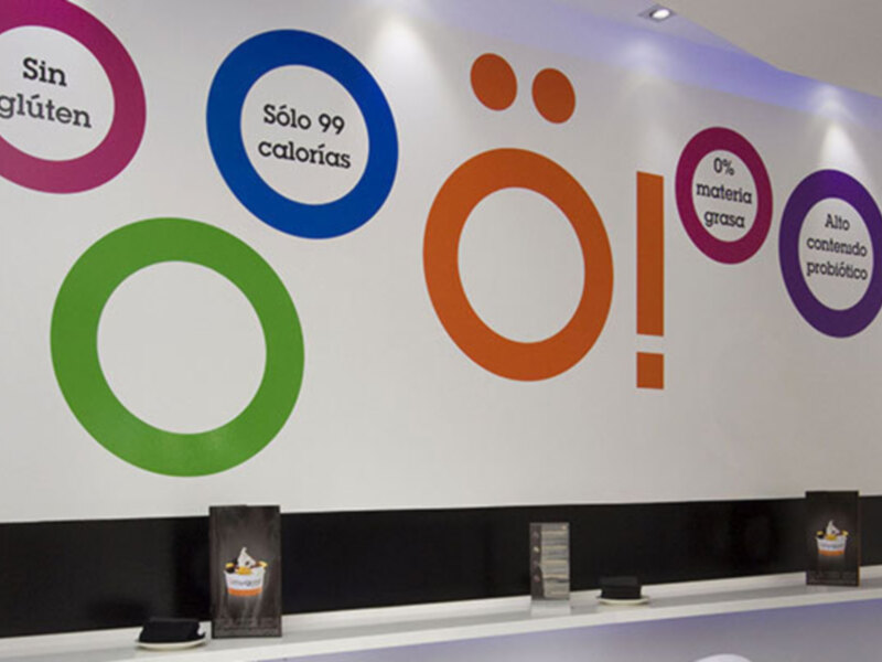 Un mostrador de recepción con un logo de marca que promete una dieta saludable, sin gluten, con solo 99 calorías, sin grasa, con 0% materia grasa, y con contenido probiótico.
