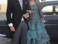 Una pareja posa frente a un coche negro, el hombre viste traje y corbata, la mujer lleva vestido largo de colores turquesa.