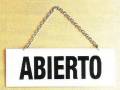 Un signo blanco con la palabra "ABIERTO" en negro, colgando de una cadena sobre un fondo amarillo.