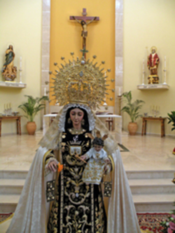Imaginaria representación de una figura religiosa vestida con traje tradicional, posiblemente una Virgen, en un entorno de iglesia con elementos decorativos y estatuas.