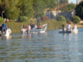 Tres personas en botes de motor navegando por un lago con vegetación y casas al fondo.