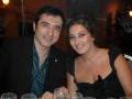 Un hombre y una mujer sonríen mientras están sentados en un restaurante con copas de vino. La imagen muestra una cena formal o una celebración en un ambiente elegante con luces suaves.