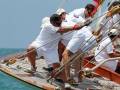 Un grupo de personas vestidas con ropa deportiva participando en un evento náutico, posiblemente una regata de vela. Los participantes están en un barco y están trabajando juntos para controlar el timón. El agua es azul claro, indicando que está en un mar abierto o bahía.