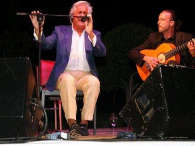 Dos músicos en un escenario al aire libre, uno con una guitarra acústica y el otro con un instrumento de viento.