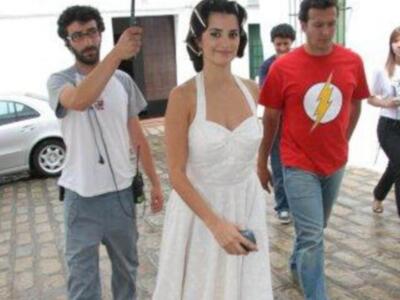 Una mujer con vestido blanco posa mientras un hombre le toma una foto. Al fondo, otros individuos caminan por el camino.