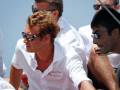 Un grupo de personas en camisetas blancas con el logo "Belle Cruise" sentadas al aire libre. Algunos llevan gafas de sol. El fondo es claro y soleado, sugiriendo un ambiente relajado o de vacaciones.