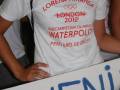 A una persona con un camiseta blanca que dice "LORENA MIRANDA LONDON 2012 SUBCAMPEONA OLIMPICA WATERPOLO PERO ERES DE ORO!!" y detrás hay una pancarta con letras azules.
