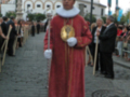 Un hombre vestido con un traje rojo y dorado, posando en una calle histórica. Detalle de la imagen: vestimenta tradicional, ambiente urbano con edificios antiguos.