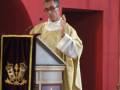 Un sacerdote oficia una ceremonia religiosa en un entorno tradicional, vestido con un hábito dorado y ante un altar con detalles ornamentales.