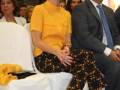 Una mujer en un traje amarillo sonriendo mientras se sienta junto a una persona de negocios.
