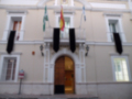 Fachada de un edificio con dos banderas españolas y un cartel indicando la dirección de la calle.
