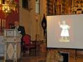 Presentación de una figura histórica en una sala de conferencias, con un orador en el podium y una proyección en el fondo.