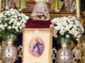 Fotografía de un altar religioso con una imagen de la Virgen en el centro, rodeada por flores blancas y detalles dorados.