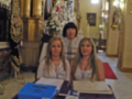 Tres personas sentadas en un altar con libros y otros objetos en un interior de iglesia decorado con adornos festivos.