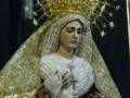 Imagen de una Virgen María vestida con un manto blanco y dorado, llevando una corona de oro y una cruz en la mano izquierda. La imagen es detallada, con texturas de seda y metal brillantes.