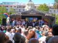 Evento público en un escenario al aire libre con una gran audiencia en un día soleado.