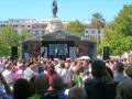 Una multitud de personas en un evento público, con una estatua en el centro y un escenario con luces en el fondo.