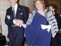 Elegante pareja en una celebración formal, con la mujer vestida con un vestido azul y el hombre con traje y corbata, ambos sonrientes y caminando juntos.