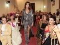 Modela caminando por la pasarela en un evento de moda, vestida con un traje de cuadros negros y blancos, rodeada de un público atento y elegante.