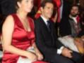 Una mujer en un vestido rojo está sentada junto a una persona en traje negro. La imagen parece ser de un evento formal, posiblemente una gala o ceremonia.
