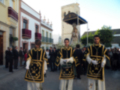 Procession with three men in traditional black and gold uniforms carrying a statue.