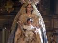Virgen María con Niño Jesús en una iglesia, vestida de blanco y dorado.