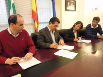 Un grupo de personas se reúnen en una sala de conferencias con banderas españolas y portuguesas. Se están sentando en una mesa con documentos, uno de ellos está firmándolos.