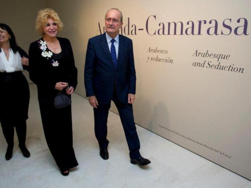 Dos personas caminan frente a una pared con letras en español y inglés que mencionan 'Arabesque y seducción'.