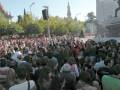 Una multitud en un evento al aire libre, con una torre visible en el fondo y un escenario grande a la derecha.