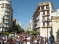 Una multitud de personas en una manifestación, con carteles y pancartas, caminando por una calle con edificios históricos a ambos lados.