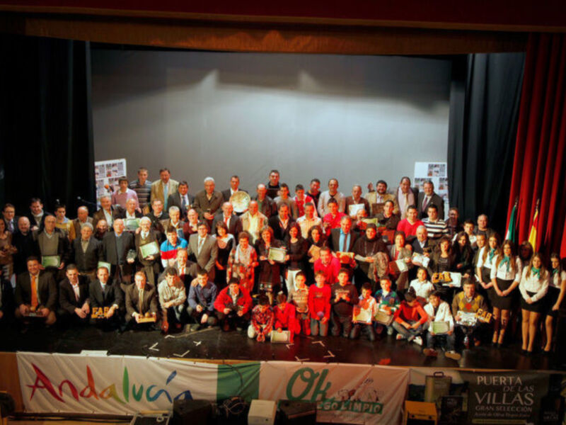 Celebración de premiados en un evento en Andalucía con banderas y carteles de patrocinio en el escenario.
